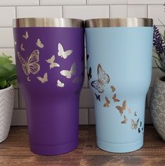 three different colored tumblers sitting next to each other on a wooden table with potted plants in the background