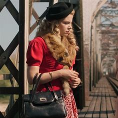 a woman in a red dress holding a black purse and standing on a train track