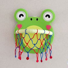 a green frog head hanging from the side of a wall with red, white and blue string attached to it