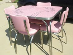 a pink table with four chairs and a car parked in the back ground behind it