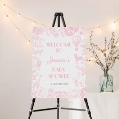 a welcome sign for a baby shower is displayed on an easel with lights in the background