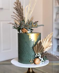 a green and gold cake decorated with feathers, flowers and acorns on a stand