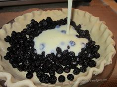 a pie topped with berries and cream being poured into it