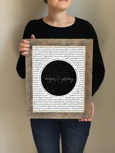 a woman holding up a framed black and white art piece with words written in it