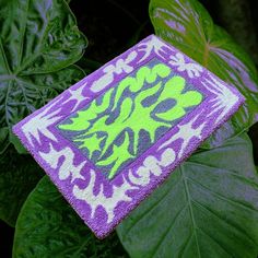 a green and purple flowered towel sitting on top of a lush green leafy plant