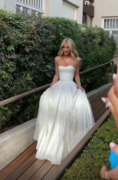 a woman in a white dress is sitting on a bench and taking a selfie