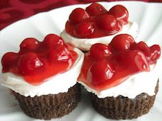 three cupcakes with white frosting and cherries on top, sitting on a plate