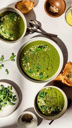 three bowls of green soup on a white table