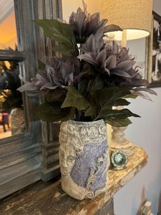 a vase filled with purple flowers sitting on top of a wooden table next to a mirror