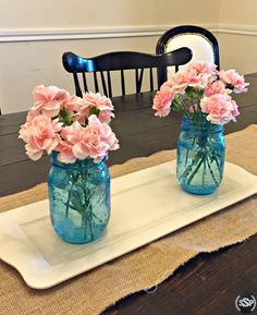 two blue mason jars with pink flowers in them sitting on a place mat next to a black chair