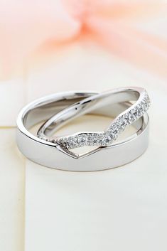 two white gold wedding rings with diamonds on top of each other in front of a pink flower