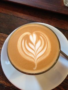 a cappuccino on a saucer with a spoon in it sitting on a wooden table