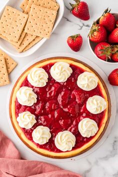 a strawberry cheesecake with whipped cream on top and strawberries in bowls around it