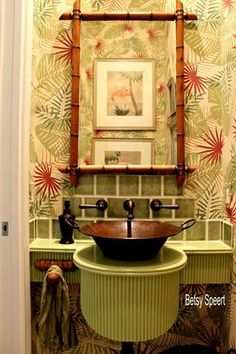 a green sink in front of a mirror and wallpaper with flowers on the walls