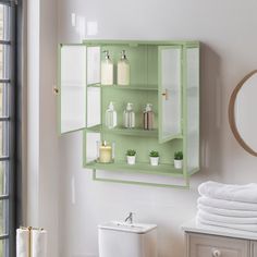 a bathroom with green cabinets and white towels on the shelf next to the toilet is shown