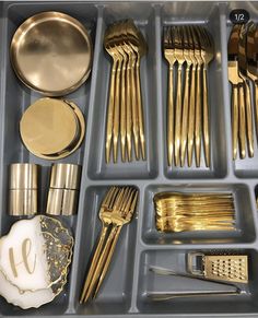 a tray filled with lots of gold colored utensils and silverware in it