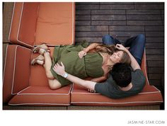 a man and woman laying on top of an orange couch with their arms around each other