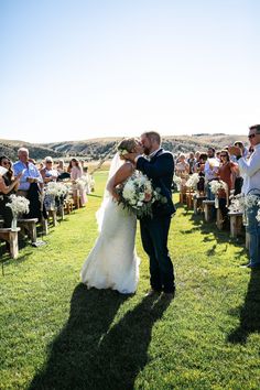 a bride and groom kissing in front of an outdoor wedding ceremony on the grass with their guests