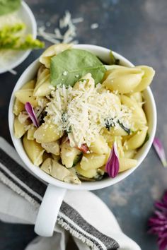 a white bowl filled with pasta and spinach on top of a table next to flowers