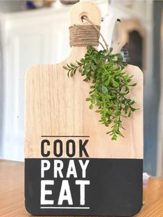 a wooden cutting board with a plant on top of it that says cook pray eat