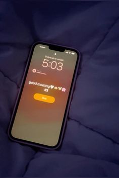 an iphone with the time displayed on it's display screen, sitting on a bed