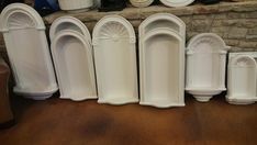 several white urinals lined up against a brick wall in a room with wood flooring