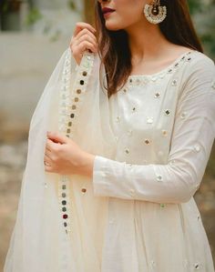 a woman wearing a white dress and jewelry with her hands on her hips, posing for the camera