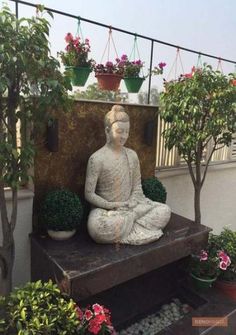 a buddha statue sitting on top of a wooden bench surrounded by potted plants and flowers