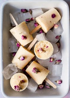 several popsicles with flowers on them sitting on ice in a white tray and one is being dipped with toothpicks