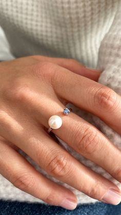 a woman's hand with a pearl and diamond ring on her left hand, wearing a white sweater