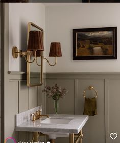 a white sink sitting under a bathroom mirror next to a wall mounted art piece with a painting on it