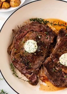 two steaks with butter and herbs on top of mashed potatoes in a white bowl