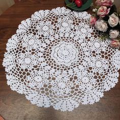 a white doily sitting on top of a wooden table next to some pink flowers