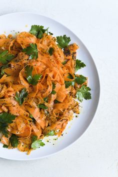 a white plate topped with pasta and garnished with parsley on the side