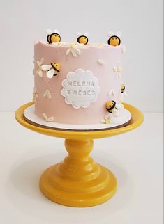 a pink cake with bees on it sitting on top of a yellow pedestal next to a white wall