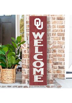 a wooden welcome sign next to a potted plant on the front door porch with brick wall