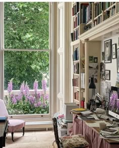 a room with lots of bookshelves and purple flowers in the window sill