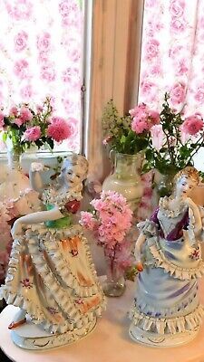 three ceramic figurines sitting on top of a table next to vases filled with flowers