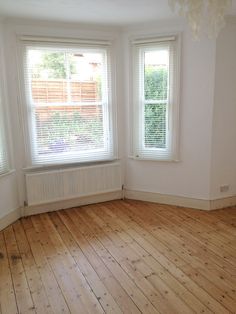 an empty room with two windows and wooden floors