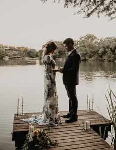 a bride and groom standing on a dock holding hands