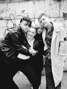 four people posing for a photo in front of graffiti