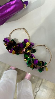 two pairs of purple and green flower hoop earrings sitting on top of a white table