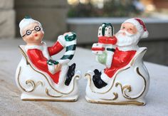 two figurines of santa claus and mrs claus sitting on sleighs