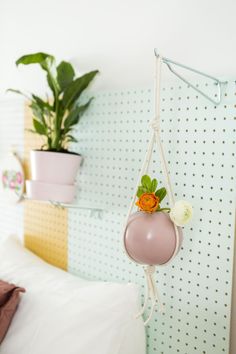 a pink hanging planter with an orange flower on it in front of a white bed