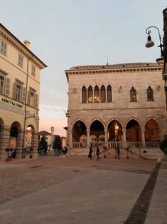 people are walking in front of an old building at sunset or sunrise, with the sun going down