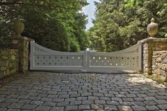 a stone driveway with a white gate surrounded by trees