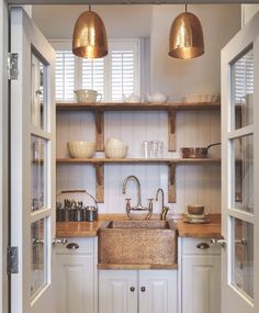 a kitchen with white cabinets and wooden counter tops, two copper lights above the sink