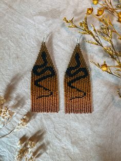 two pairs of beaded earrings sitting on top of a white table next to dried flowers