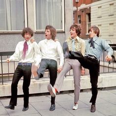 four young men are standing on the sidewalk in front of a building and one man is holding his leg up