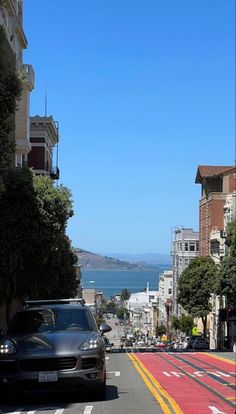 a car driving down a street next to tall buildings and the ocean in the background